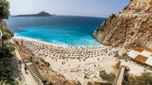 A panoramic view of Antalya's stunning coastline, with azure waters gently lapping against golden sandy beaches, framed by lush green mountains and ancient ruins in the distance